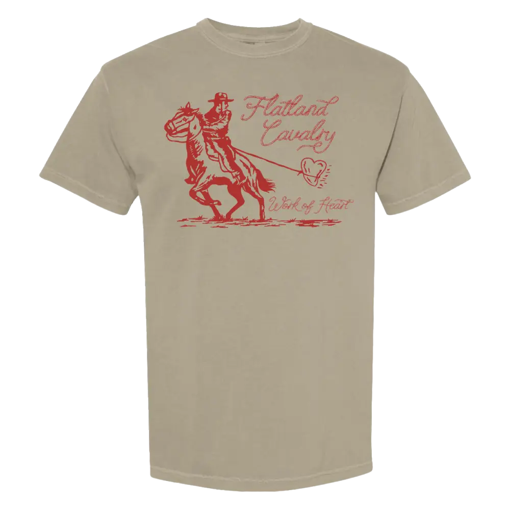 Beige short-sleeved t-shirt featuring a red graphic of a cowboy on horseback with the text ’flatland cavalry’ and ’work of heart.’