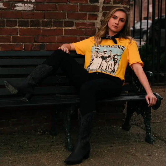 Woman wearing a yellow t-shirt with a graphic print, sitting on a bench.