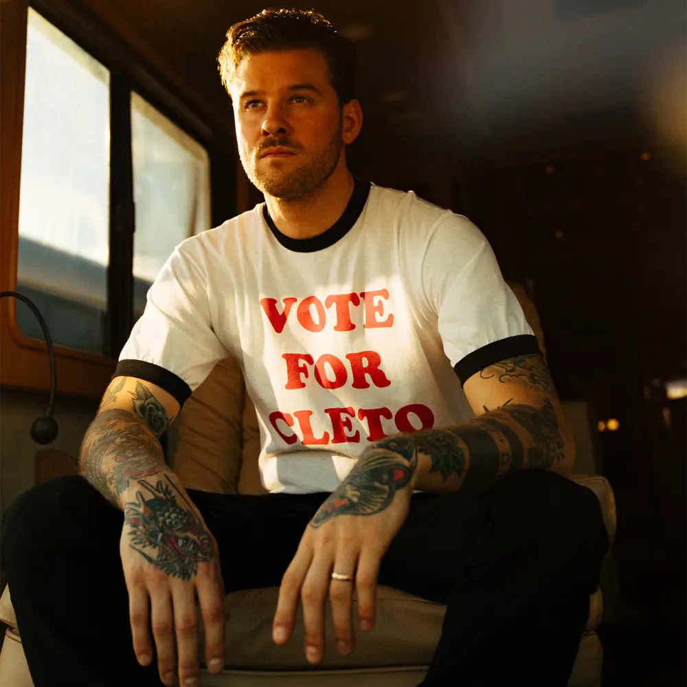 Man wearing a white t-shirt with red text saying ’VOTE FOR CLETO’.
